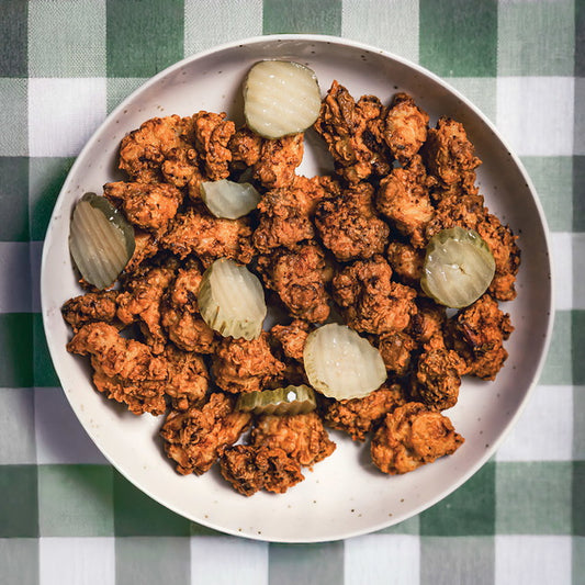 Fried chicken with pickles on a white plate over a green and white checkered tablecloth