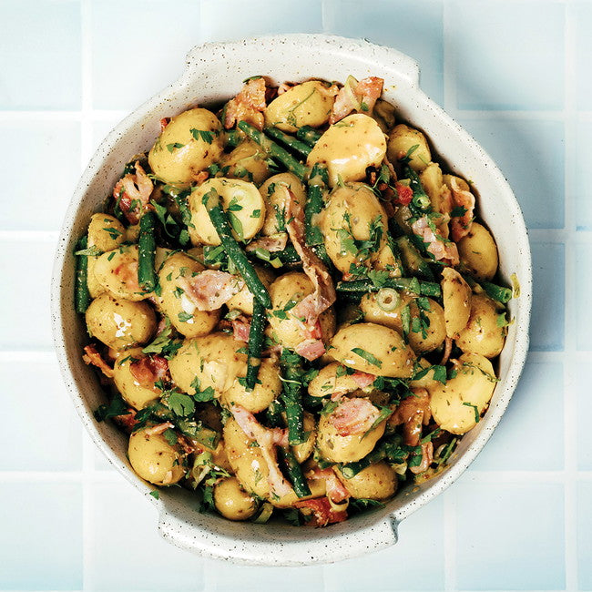 Potato salad with green beans and bacon in a white bowl on a light blue tiled background