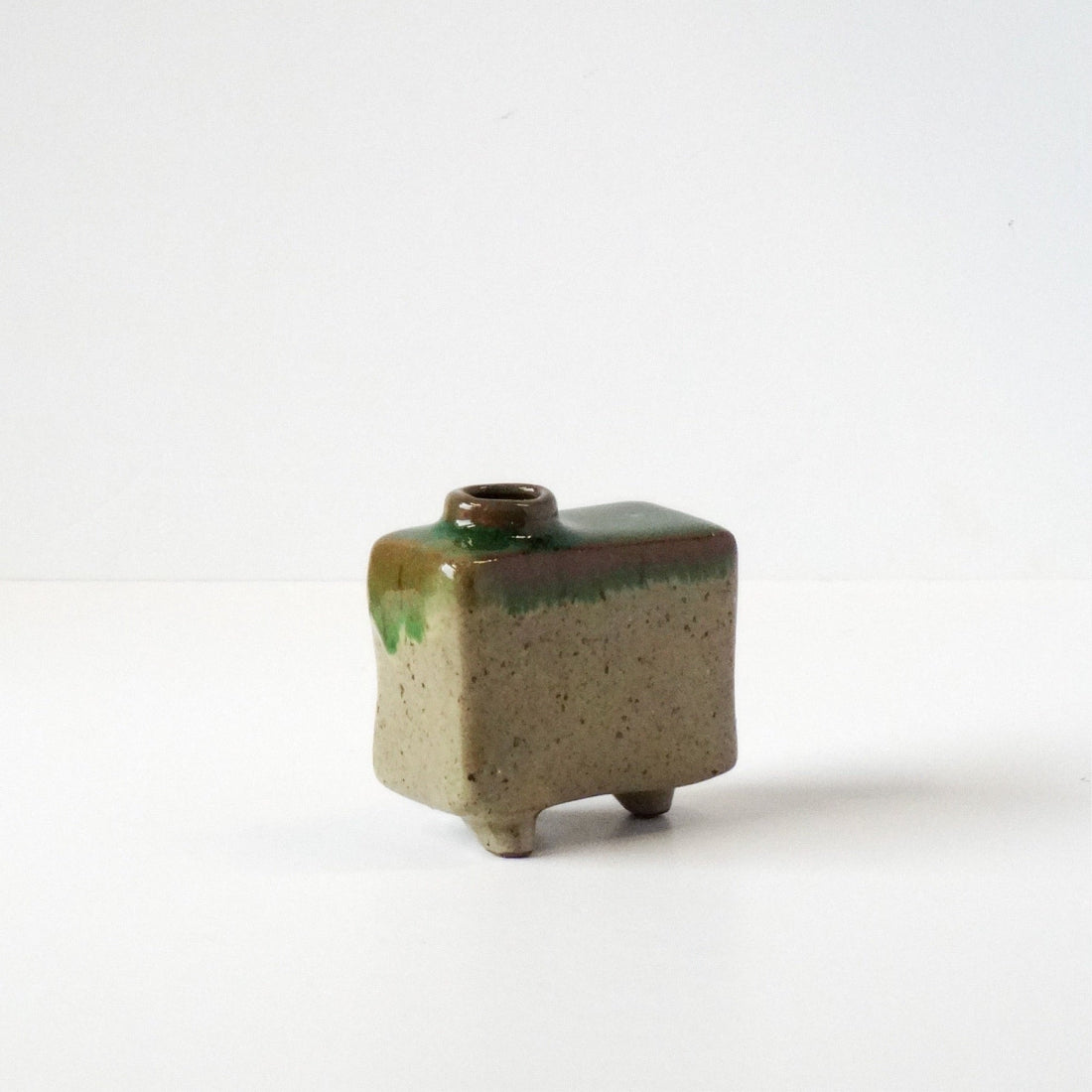Small square ceramic vase with green and brown glaze on a white background