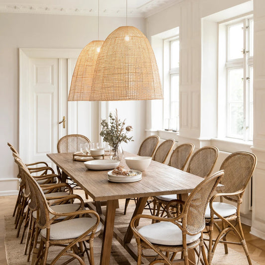 Two rattan lampshades hanging over dining wooden table and chairs on a wooden floor.