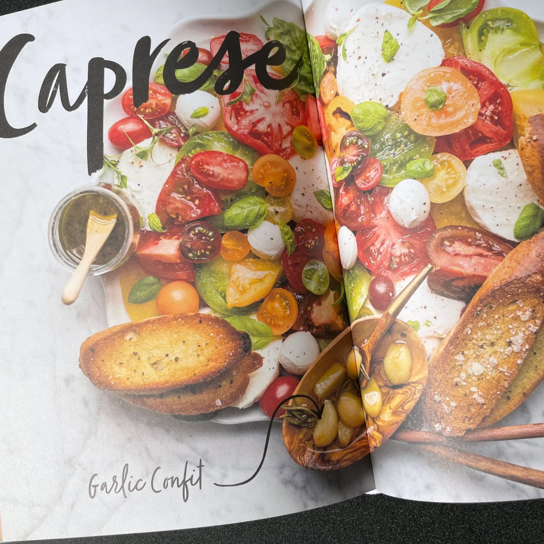 Open book with Caprese salad and garlic confit food on a marble surface