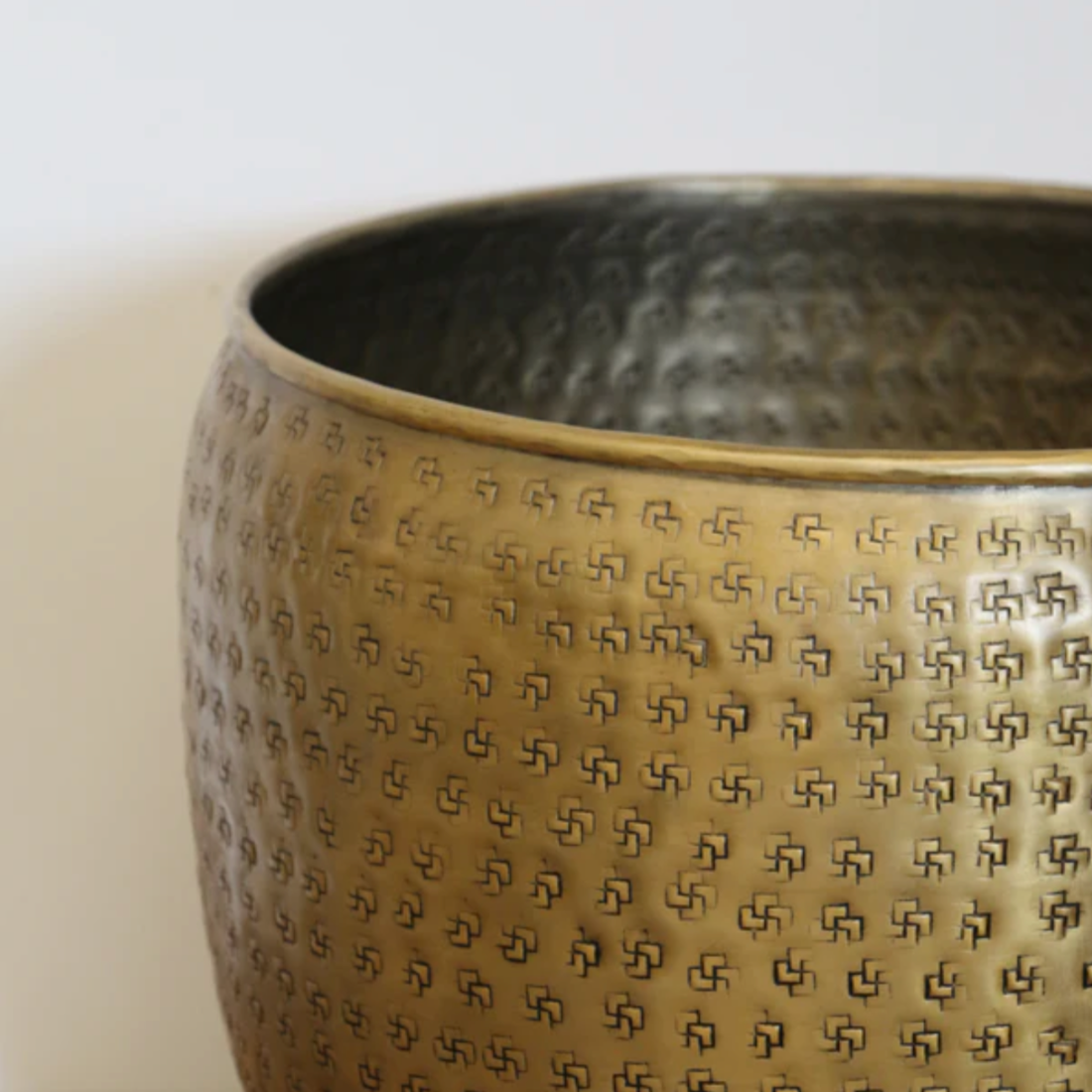 Close up of a textured geometric pattern on an antique brass planter against a light background