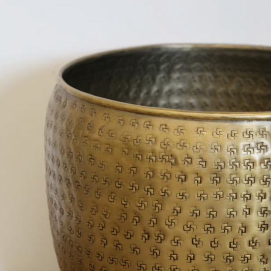 Close up of a textured geometric pattern on an antique brass planter against a light background