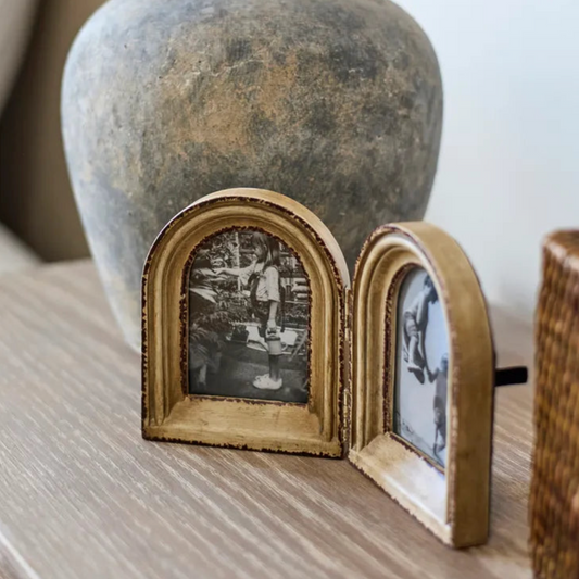 Double arch photo frame on wood surface in front of a rustic vase