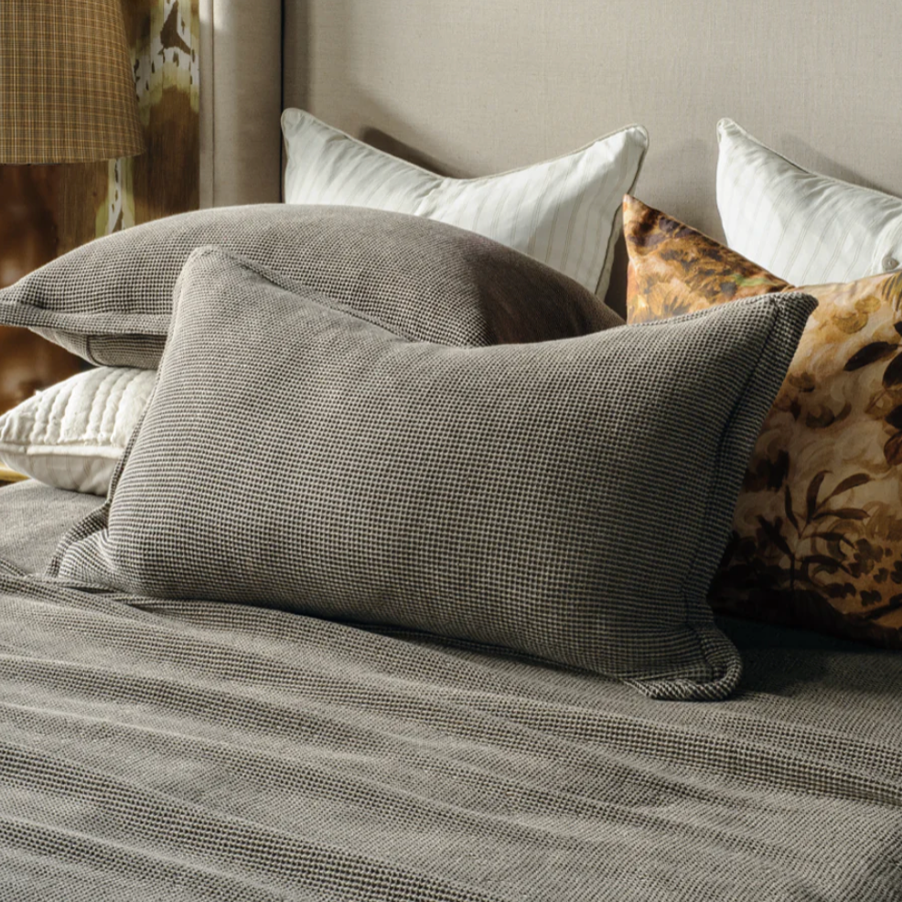 Bed with gray bedding and pillows against a patterned wall.