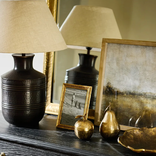 Decorative setting with black lamps, gold apples, and a framed picture on a dark surface.
