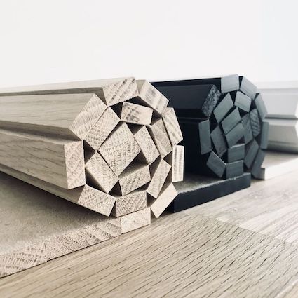 Two wooden arm chair side rests, one natural finish and one with a black edge detail, placed on a wooden floor.