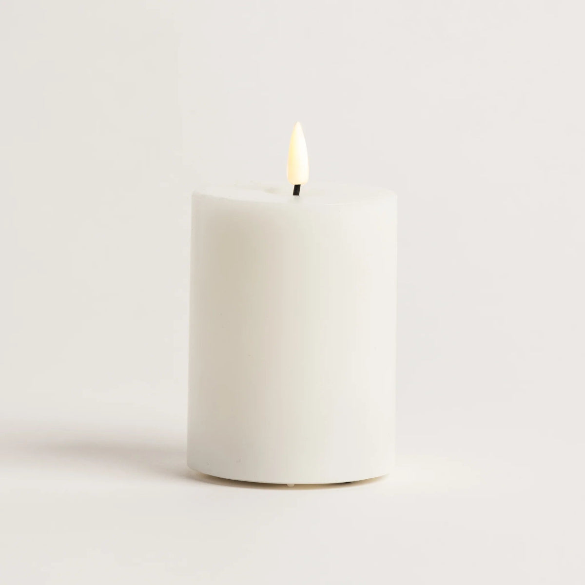 White candle with a lit wick on a light gray background