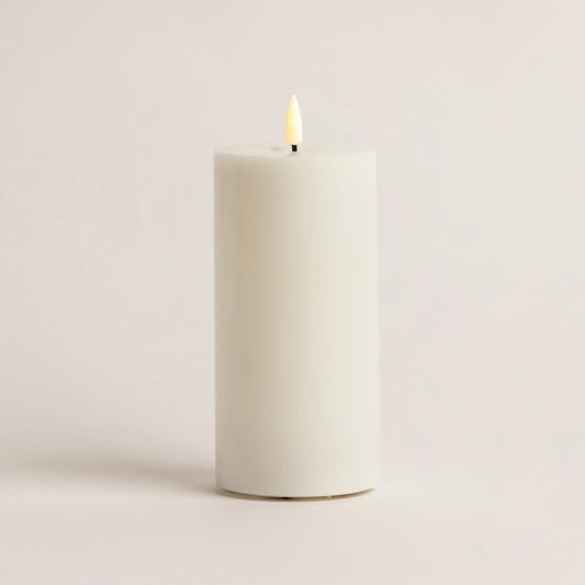 White candle with a lit wick on a light beige background