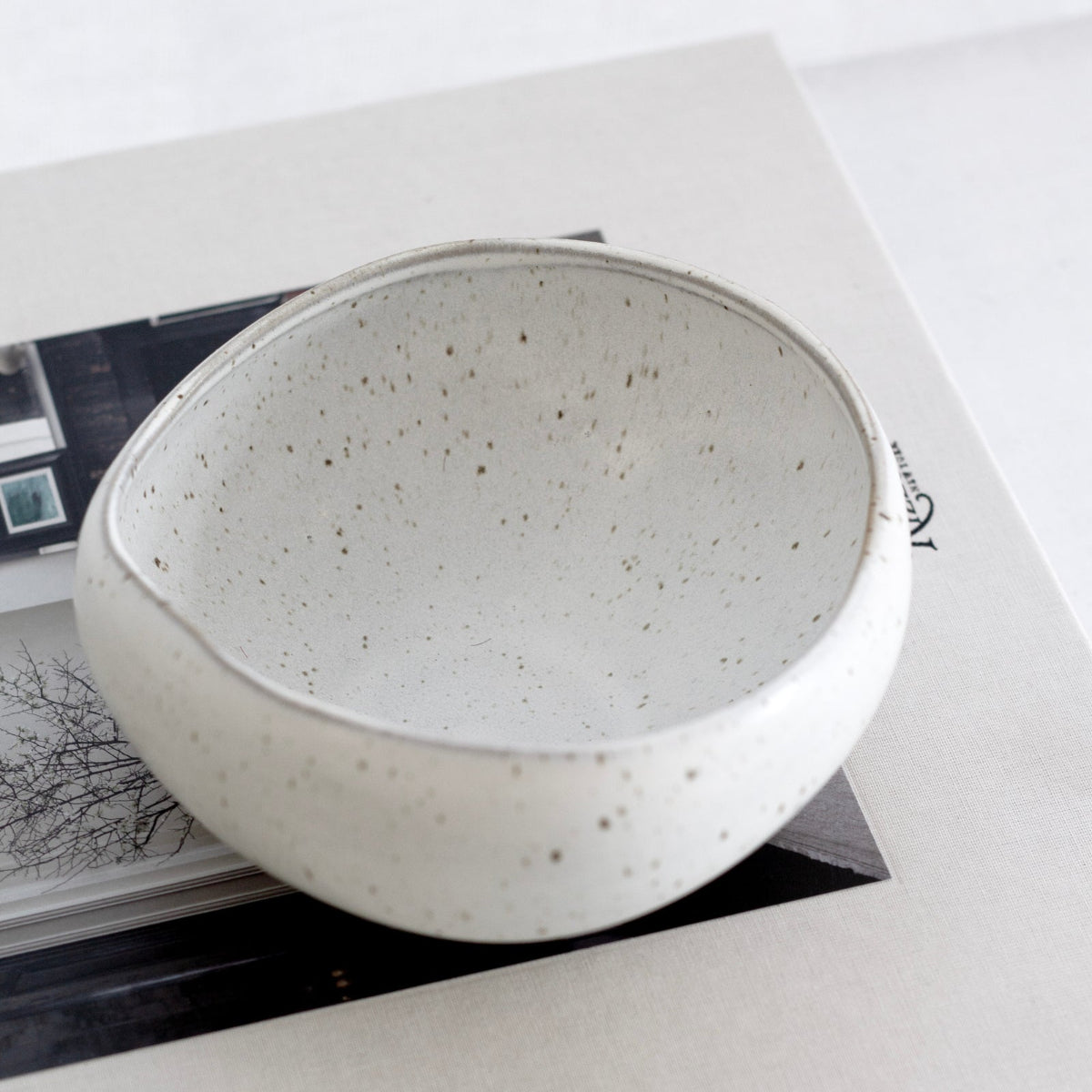 Speckled ceramic bowl on top of a book titled 'Interiors' with a white background