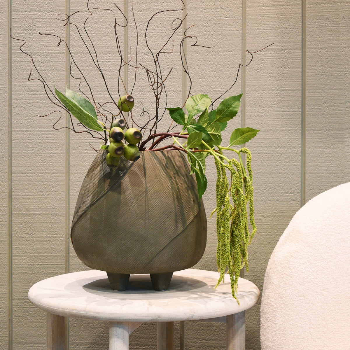 Decorative vase with plants on a small round table against a neutral wall.