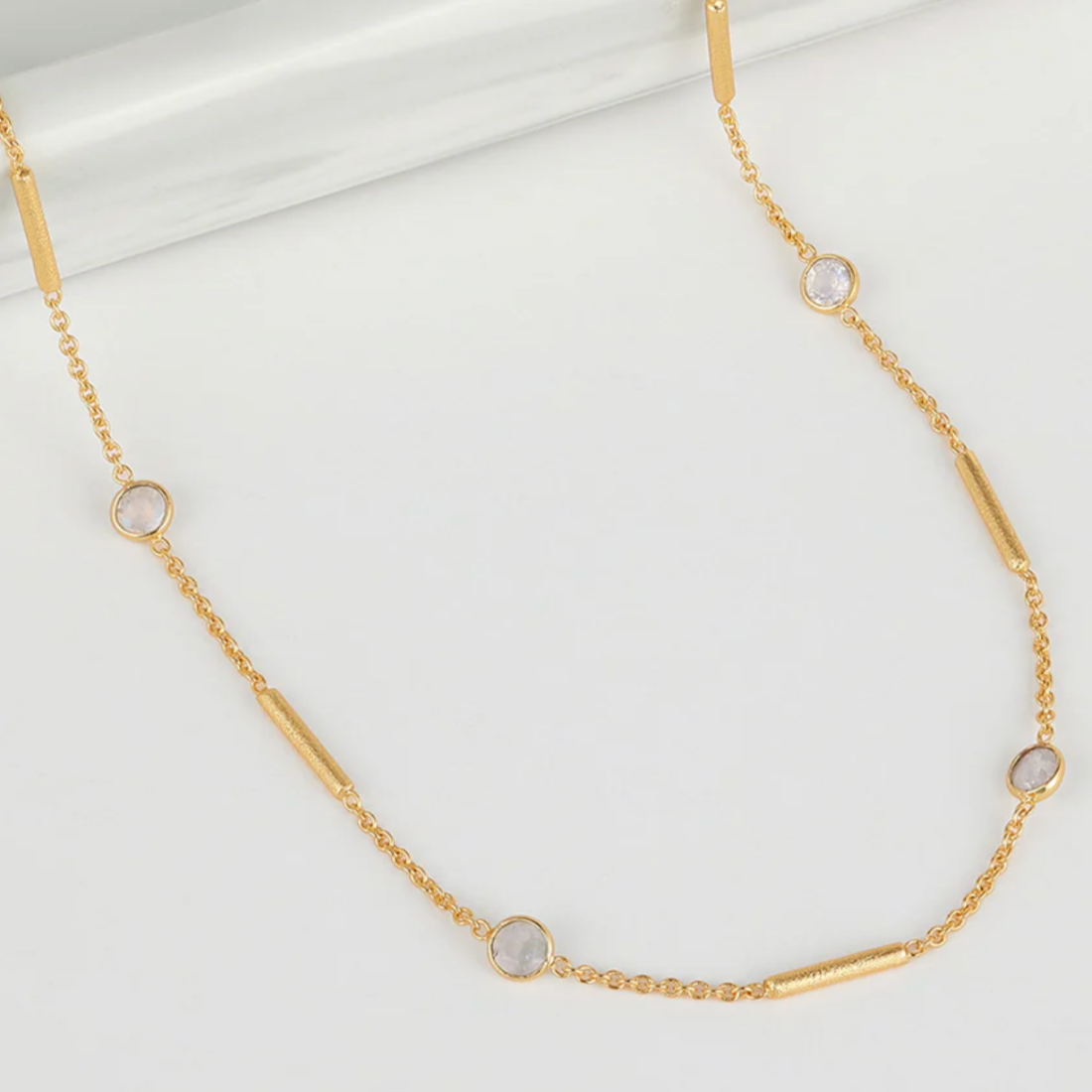 Gold necklace with small round moonstones on a white background