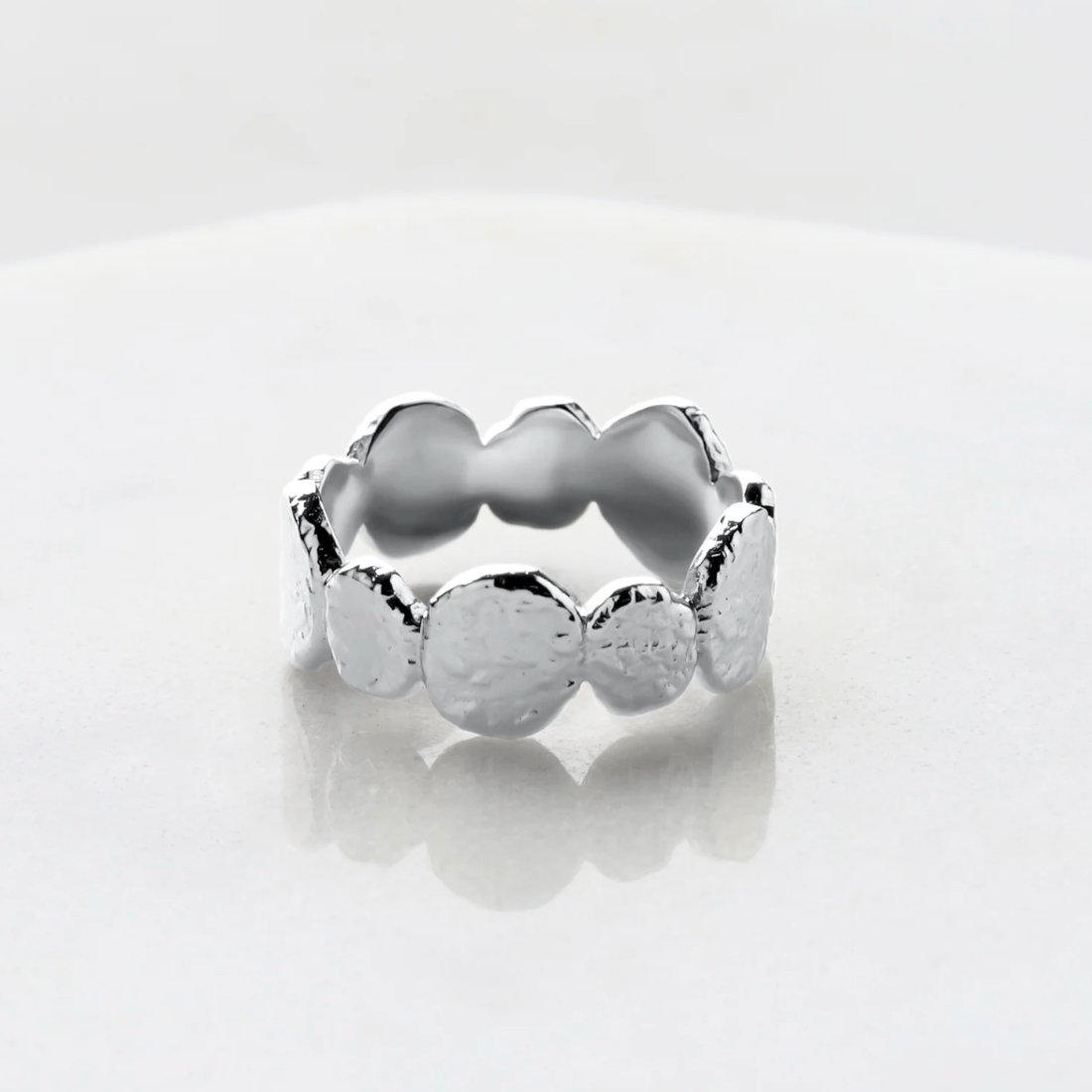 Silver ring with hammered textured design on a light gray background