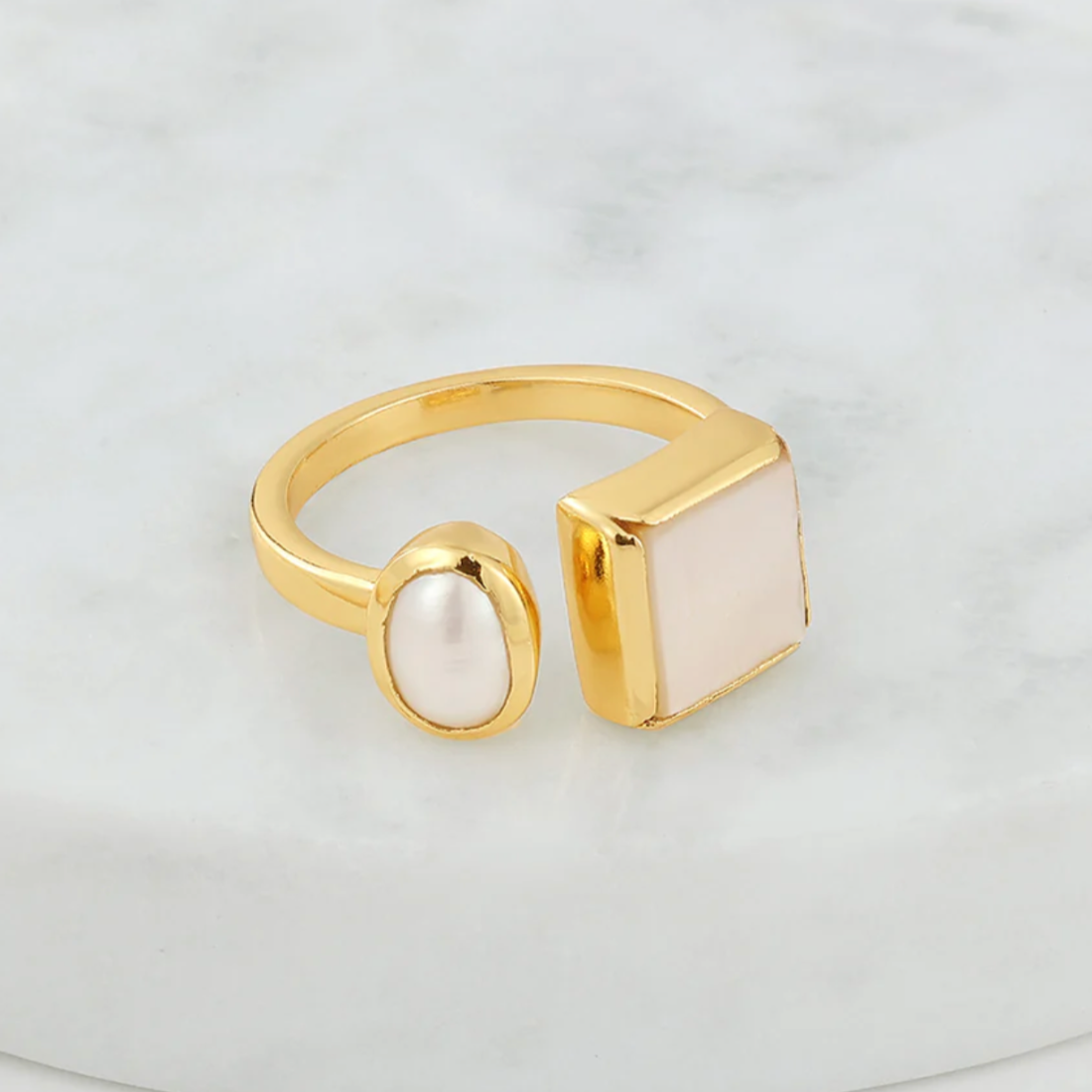 Gold ring with a square pearl stone and oval pearl on a white background