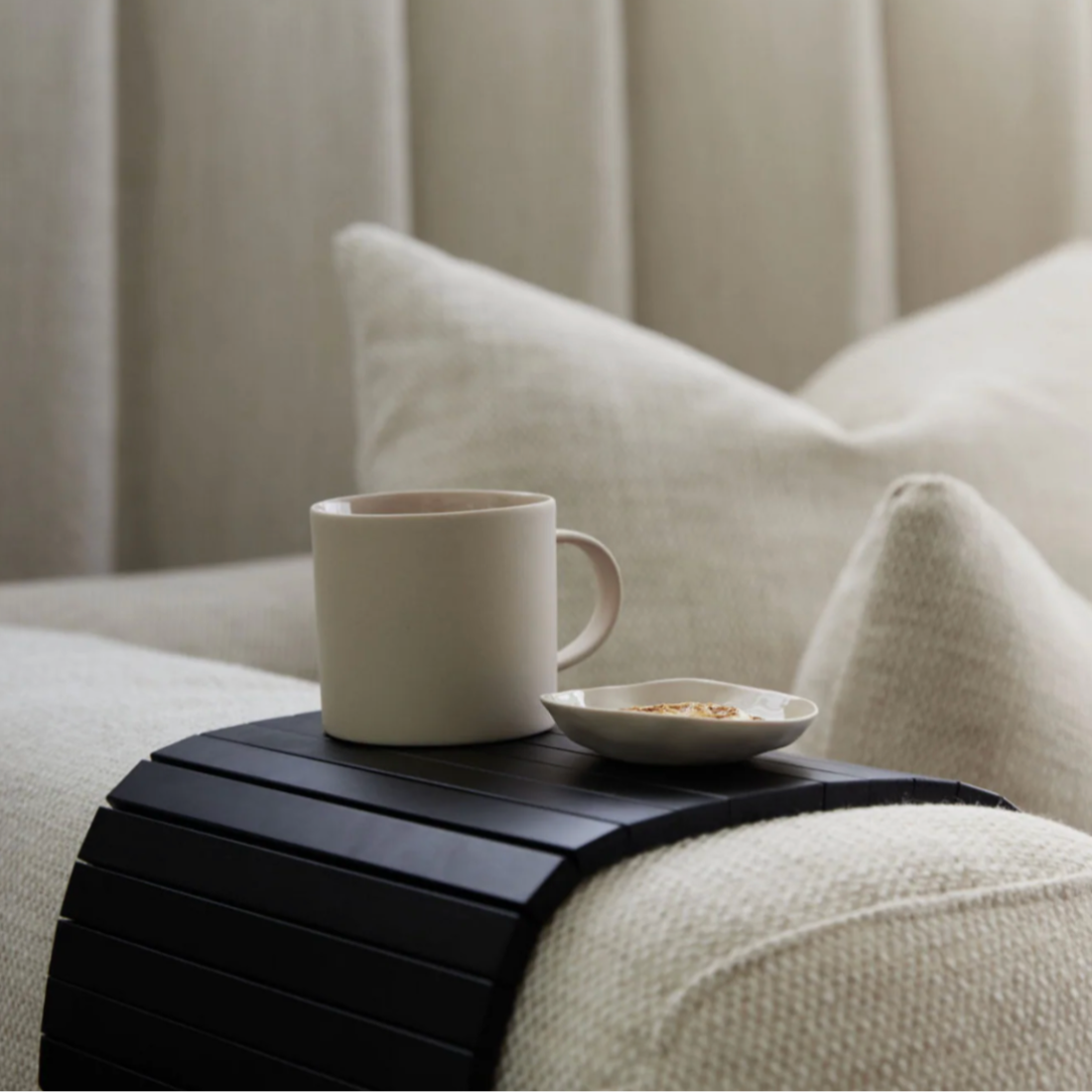 Black armchair rest with a white mug and small dish on a beige couch.