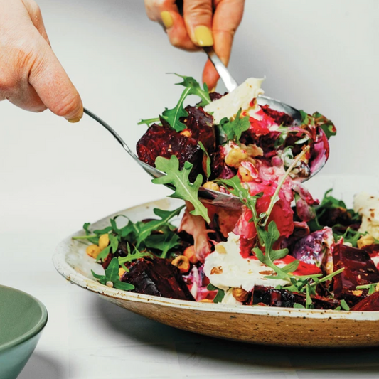 Person picking up a salad with a fork from a bowl on a light background