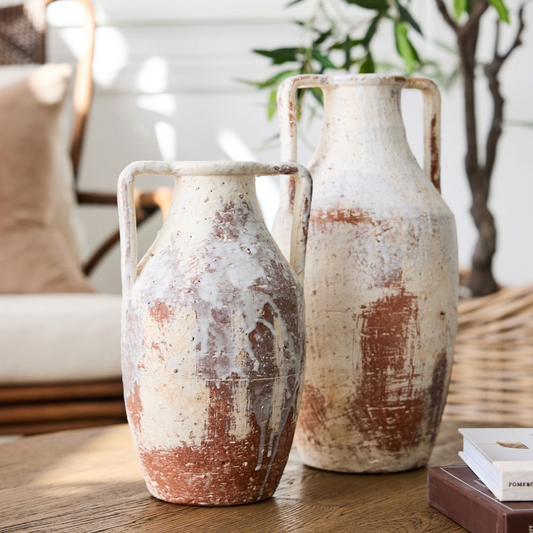 Two rustic ceramic vases on a wooden surface with a blurred indoor background