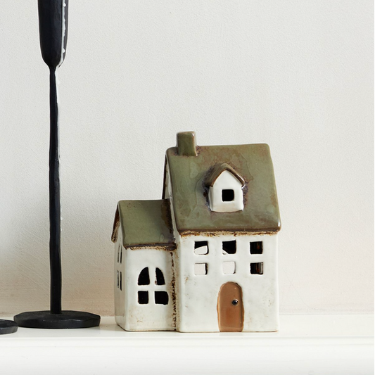 Ceramic chapel house with green roof on a white surface with a candle holder to the side.
