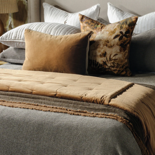 Neatly made bed with decorative pillows and a textured headboard against a patterned wall.