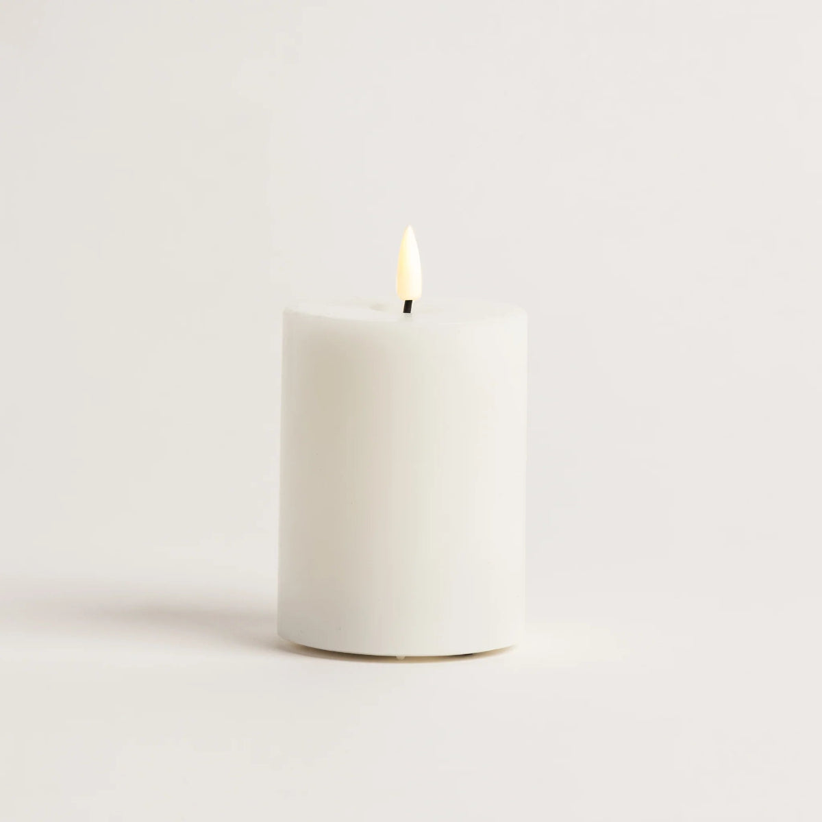 White candle with a lit wick on a light beige background