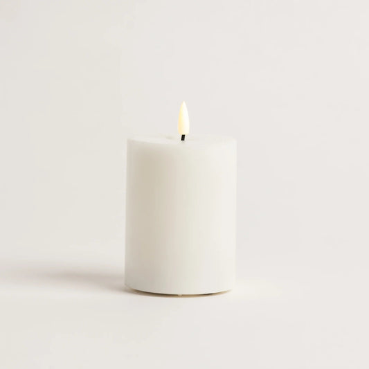 White candle with a lit wick on a light beige background