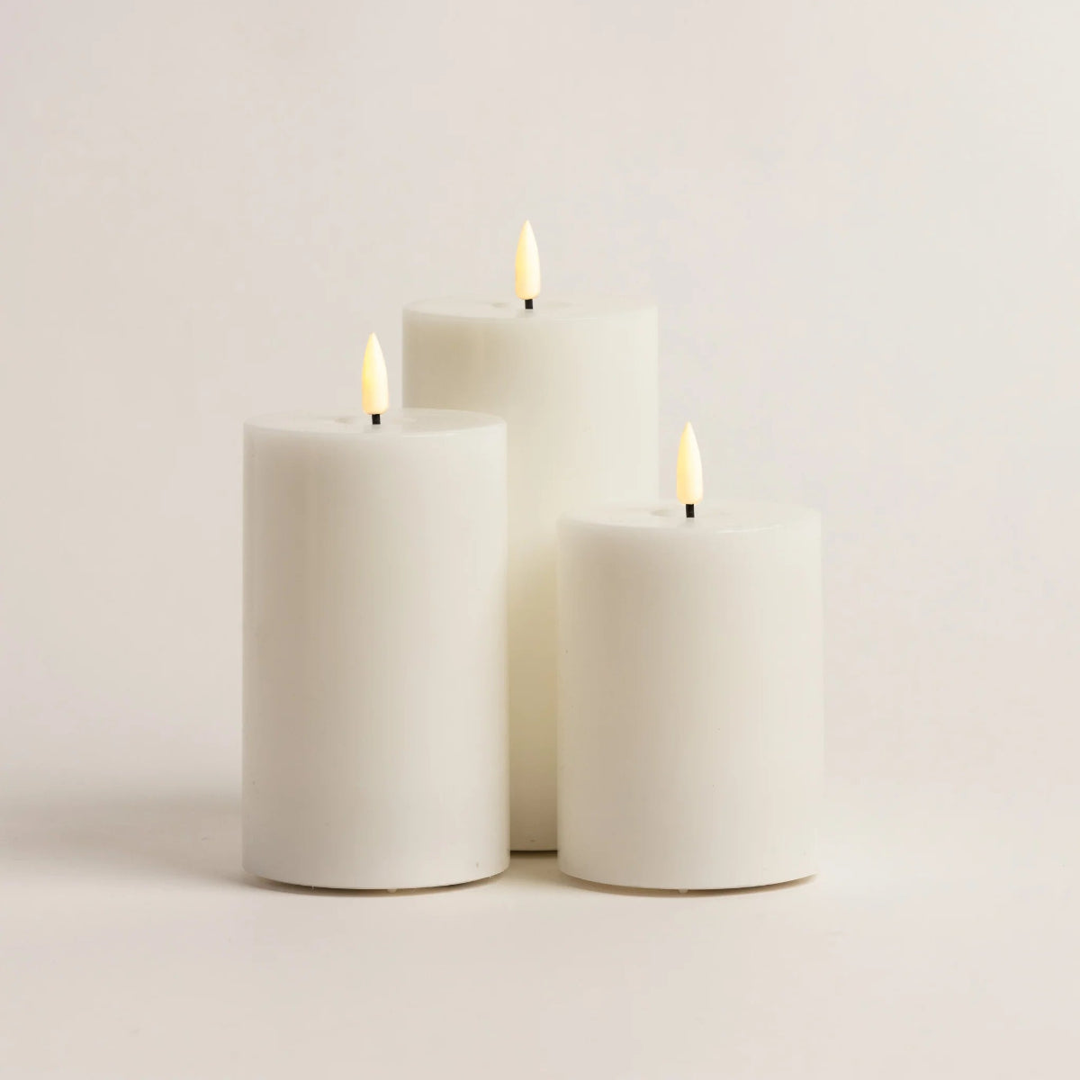 Three white candles with lit wicks on a light gray background